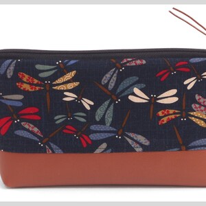 May include: A navy blue zippered pouch with a brown leather bottom. The pouch is decorated with a repeating pattern of colorful dragonflies.