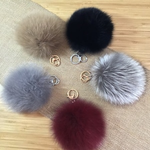 May include: Five fluffy fur pom pom keychains in different colors: beige, black, gray, burgundy, and silver. Each pom pom is attached to a gold key ring.