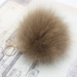 May include: A brown fluffy pom pom keychain with a gold metal key ring.