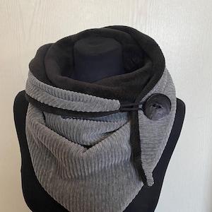 Può includere: Una sciarpa infinita grigia e nera con chiusura a bottone. La sciarpa è realizzata in un tessuto morbido e a coste.