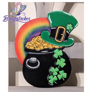 May include: A black pot filled with gold coins, topped with a green leprechaun hat with a gold buckle and a shamrock. A rainbow with glitter is behind the pot.