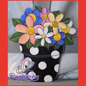 May include: A black flower pot with white polka dots, filled with a bouquet of colorful flowers. The flowers are pink, yellow, blue, and white. The pot is painted with a whimsical style.