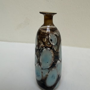 Può includere: Un vaso decorativo in vetro con bordo marrone e corpo con un motivo di forme organiche marroni, blu e bianche. Il vaso ha un collo sottile e un corpo arrotondato, adatto per esporre fiori o come elemento decorativo.