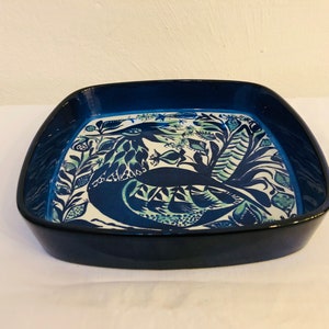 May include: A square, ceramic serving dish with a dark blue exterior and a white interior featuring a detailed illustration of a bird and foliage in shades of blue and green. The dish has rounded corners and a glossy finish.