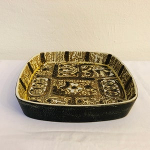 May include: A square ceramic serving dish with a black rim and a white interior. The dish is decorated with a black and brown geometric pattern.