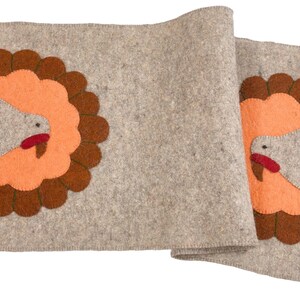 May include: A gray felt table runner with two embroidered turkeys. Each turkey is brown, orange, and red with a white body and a brown tail.