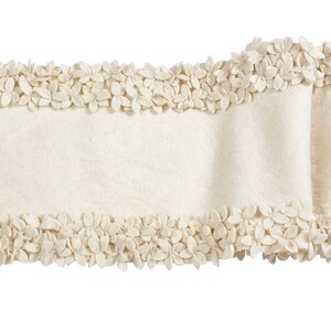 May include: A cream-colored table runner with a decorative border of small, flower-shaped embellishments.
