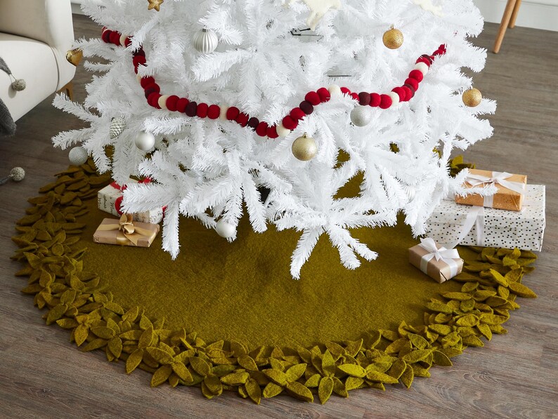 May include: A green felt Christmas tree skirt with a leafy border. The skirt is decorated with felt leaves and is placed under a white artificial Christmas tree.