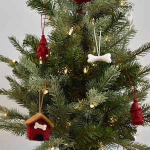 May include: A small artificial Christmas tree decorated with felt ornaments. The ornaments are shaped like dog houses and bones. The tree is decorated with white lights.