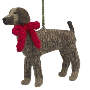 May include: A brown and white knitted dog ornament with a red bow. The ornament is hanging from a green string.