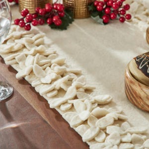 May include: A white felt table runner with a decorative scalloped edge. The runner is adorned with a row of white felt flowers along the edge.