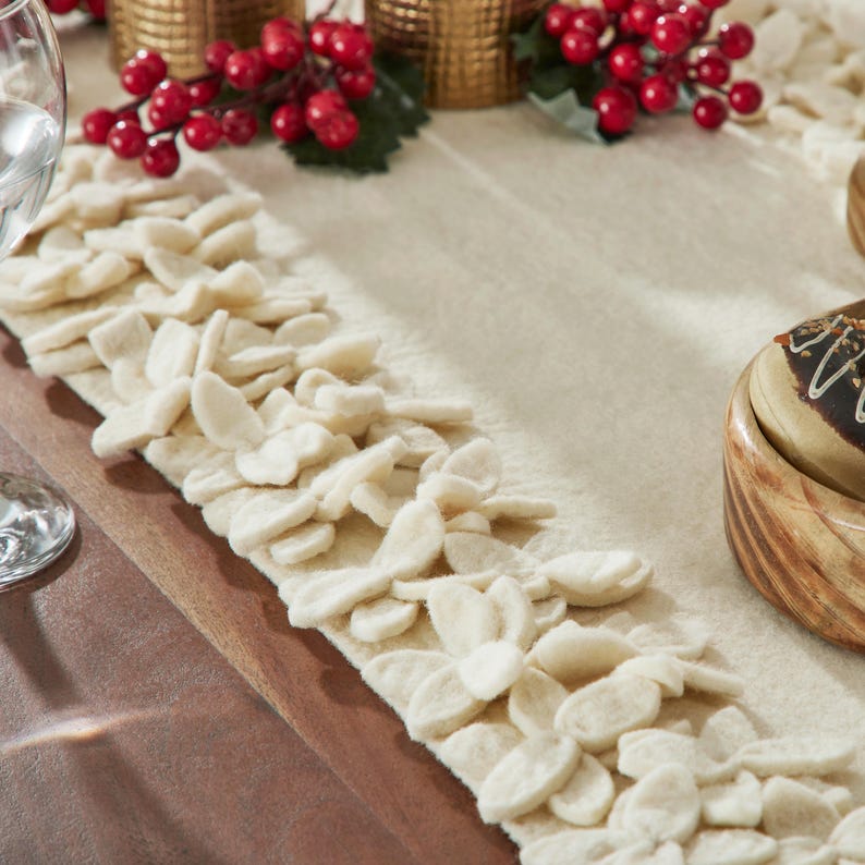 May include: A white felt table runner with a decorative scalloped edge. The runner is adorned with a row of white felt flowers along the edge.