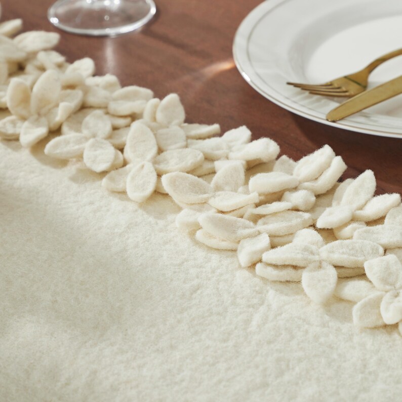 May include: A white table runner with a decorative border of white felt flowers. The runner is made of a soft, fuzzy material.