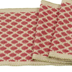 May include: A red and white table runner with a diamond pattern. The runner has a green stitched edge.