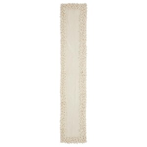 May include: A white table runner with a textured, floral design along the edges.