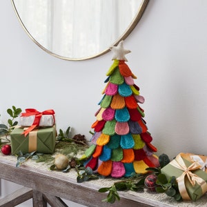 May include: A conical Christmas tree decoration constructed from layered, multi-colored felt petals in shades of green, blue, orange, pink, and yellow. The tree is topped with a small, light-colored fabric star and features a textured, soft appearance.