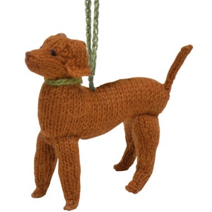 May include: A brown knitted dog ornament with a green string for hanging. The dog is standing on all four legs and has a green knitted collar.