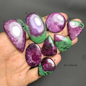 Op de afbeelding: Acht gepolijste robijn-zoisiet cabochons in diverse vormen en maten, genummerd van 1 tot 8, met levendige magenta-roze robijninsluitingen in een groene zoisiet matrix. De tekst 41-25mm is zichtbaar in de rechterbenedenhoek van de afbeelding.