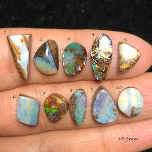 Puede incluir: Una colección de diez piedras preciosas de ópalo pulidas en varias formas y colores, incluyendo blanco, azul, marrón y verde. Las piedras preciosas miden entre 15 y 9 mm.