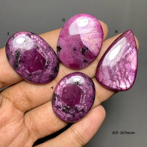 May include: Four polished ruby zoisite cabochons with magenta and black inclusions, labeled 1 through 4. The stones feature oval and teardrop shapes with smooth, reflective surfaces. The text 35-30mm is visible in the bottom right corner.