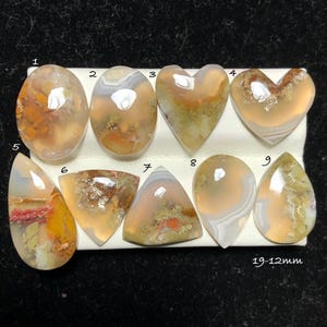 May include: Nine polished cabochon gemstones arranged in two rows, numbered 1 through 9. These translucent stones feature varied inclusions in shades of orange, yellow, and green, with some showing banded patterns. The text 19-12mm is visible.