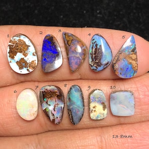 May include: A collection of ten polished opal gemstones in various shapes and colors, including blue, brown, white, and green. The gemstones range in size from 13 to 8mm.