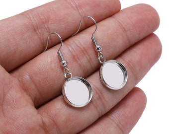 Può includere: Un paio di basi per orecchini in argento con cabochon rotondi in vetro trasparente. Gli orecchini sono su uno sfondo bianco.
