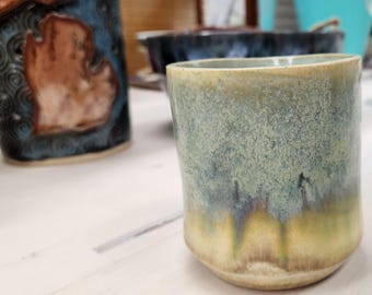 Könnte beinhalten: Eine Keramiktasse mit einer hellgrünen Glasur und einer gesprenkelten Textur. Die Glasur hat einen gelben und braunen Farbverlauf am Boden.