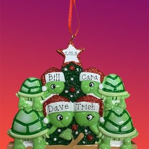 May include: A green and brown Christmas ornament featuring four turtles wearing Santa hats and standing around a Christmas tree. The tree has a star on top with the year 2023 written on it. The turtles are labeled with the names Bill, Cara, Dave, and Trish.