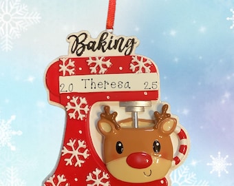 May include: A festive Christmas ornament shaped like a red stand mixer, adorned with snowflakes. The mixer features a reindeer face and the words "Baking" and "Spirits Bright". Includes the name "Theresa" and the numbers 2.0 and 25.