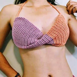 Op de afbeelding: Een gehaakt bikini-topje met een roze en oranje kleurschema. De top heeft een gekruist ontwerp aan de voorkant.