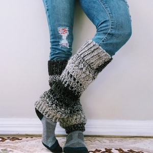 Puede incluir: Un par de calentadores de piernas de crochet gris y negro sobre un fondo de mezclilla desgastado.