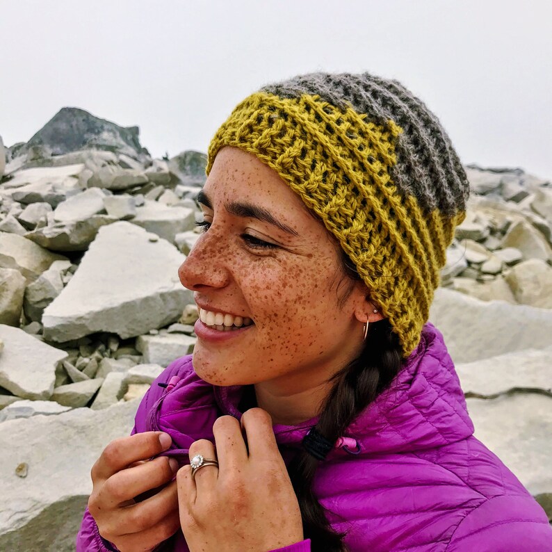 Puede incluir: Una mujer con un gorro de punto amarillo y gris y una chaqueta morada. Est&aacute; sonriendo y tiene pecas.