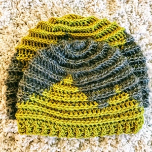 Puede incluir: Un gorro de crochet con un dise&ntilde;o texturizado en tonos verdes y grises.