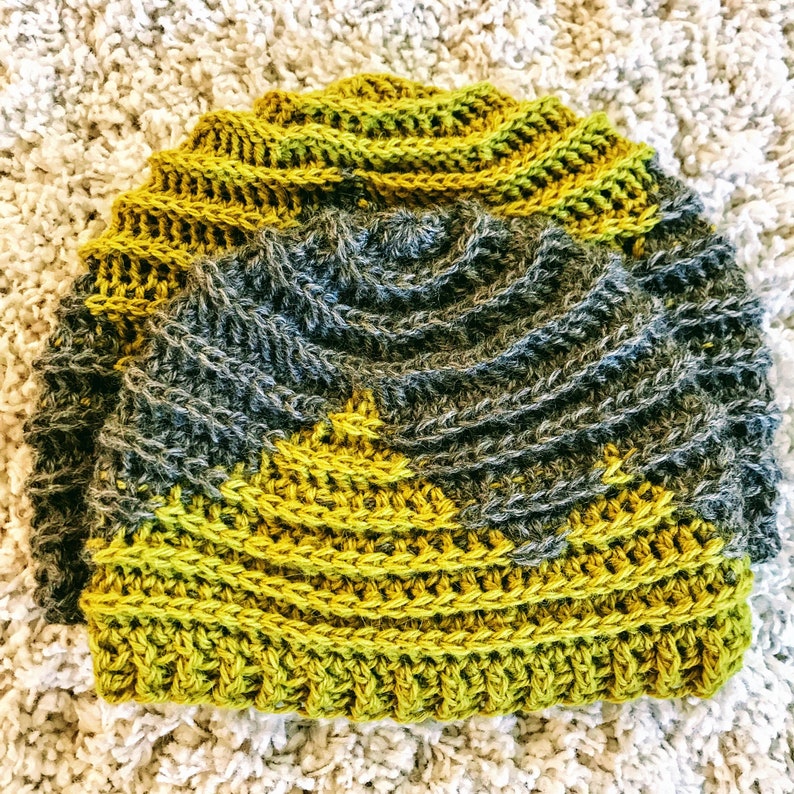Puede incluir: Un gorro de crochet con un dise&ntilde;o texturizado en tonos verdes y grises.