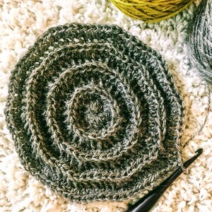 Puede incluir: Primer plano de una espiral de ganchillo en tonos marrones y verdes. La espiral se est&aacute; trabajando con un gancho de ganchillo.