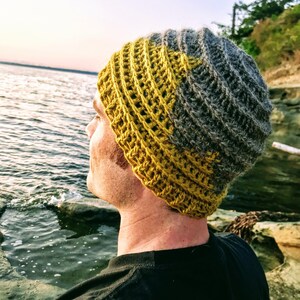 Puede incluir: Una persona lleva una boina de punto de color amarillo y gris. La boina tiene un dise&ntilde;o texturizado y est&aacute; hecha de hilo.