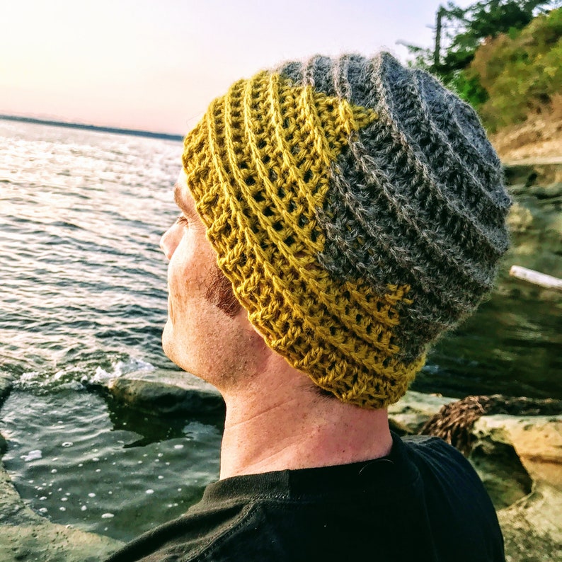 Puede incluir: Una persona lleva una boina de punto de color amarillo y gris. La boina tiene un dise&ntilde;o texturizado y est&aacute; hecha de hilo.