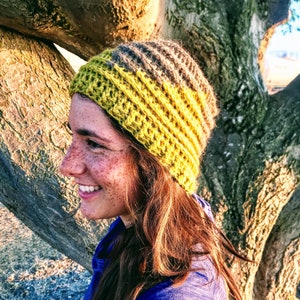 Puede incluir: Una mujer con un gorro de punto de color amarillo y gris. El gorro tiene un ala ancha y est&aacute; hecho con un hilo grueso.