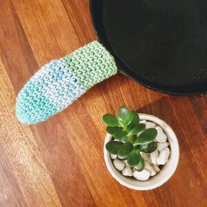 May include: A blue and green crocheted pot holder with a succulent plant in a white pot with white stones.