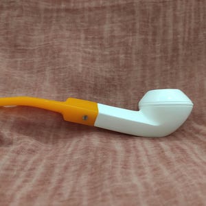 May include: A white and orange pipe with a rounded bowl. The pipe is made of a smooth, white material and has a bright orange mouthpiece.