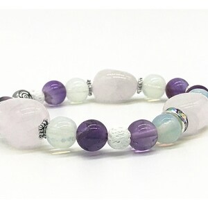 May include: A bracelet made with pink, purple, and white beads. The bracelet has a silver clasp and a silver bead with a swirl design.