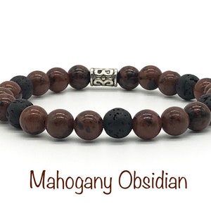 May include: A brown and black beaded bracelet with a silver charm. The beads are made of mahogany obsidian and lava rock. The bracelet is called "Mahogany Obsidian".