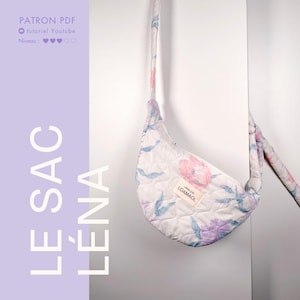 Puede incluir: Una bolsa blanca acolchada con estampado floral y una flor rosa y blanca en la parte delantera. La bolsa tiene una correa larga y una etiqueta que dice "LOAMAOL".