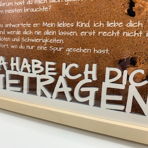 May include: A framed print with a white background and a brown corkboard texture. The print features a white text overlay that reads "Da habe ich dich getragen." which translates to "There I carried you."