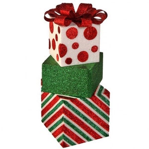 May include: A stack of three Christmas gift boxes. The top box is white with red polka dots and a red bow. The middle box is green with glitter. The bottom box is red and green striped.