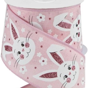 May include: A roll of pink ribbon featuring a repeating pattern of white bunny faces with glittery pink ears and cheeks, along with small white flowers and dots. The ribbon is ideal for Easter or spring crafts.