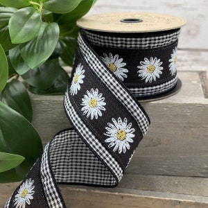 May include: Black and white gingham ribbon with a row of white daisies with yellow centers. The ribbon is on a spool.
