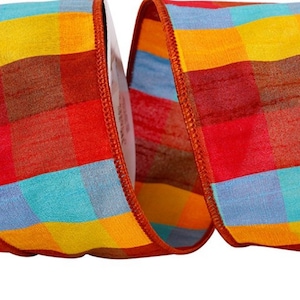 May include: A roll of orange, red, yellow and blue plaid ribbon with a brown edge. The ribbon is on a white spool.