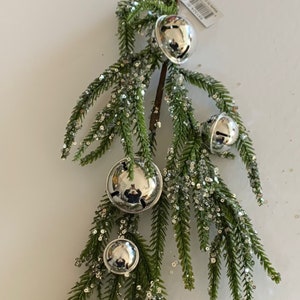 May include: A silver bell garland with four bells on a green twig with silver glitter.